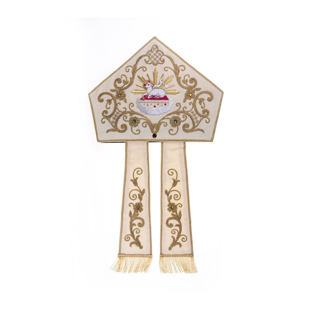 La "Mitria Agnus Dei Ricamata a Macchina" è una mitra vescovile ricamata in oro e bianco con disegno di agnello e croce, con due lappetti pendenti.