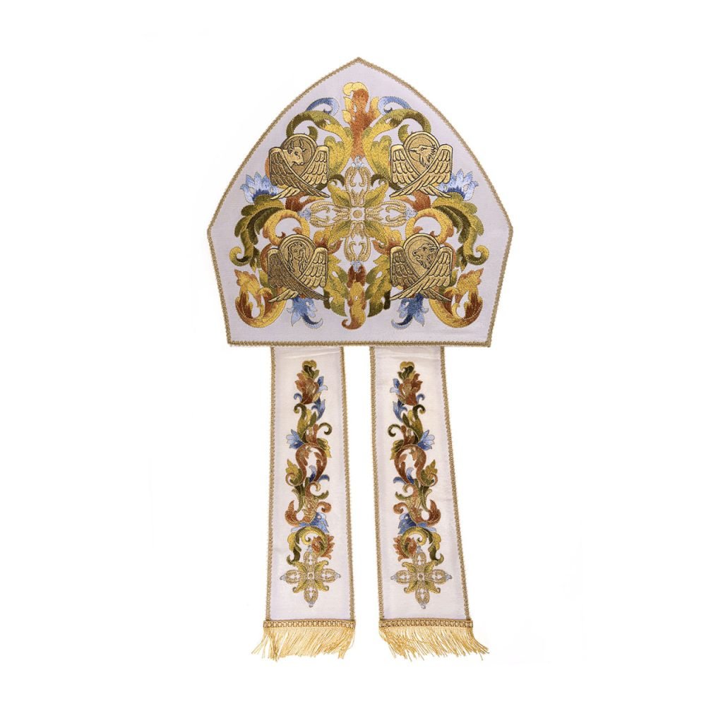 La Mitria 4 Evangelisti Ricamata a Macchina è una mitra vescovile bianca e oro con disegni floreali ricamati a macchina e due nappe.