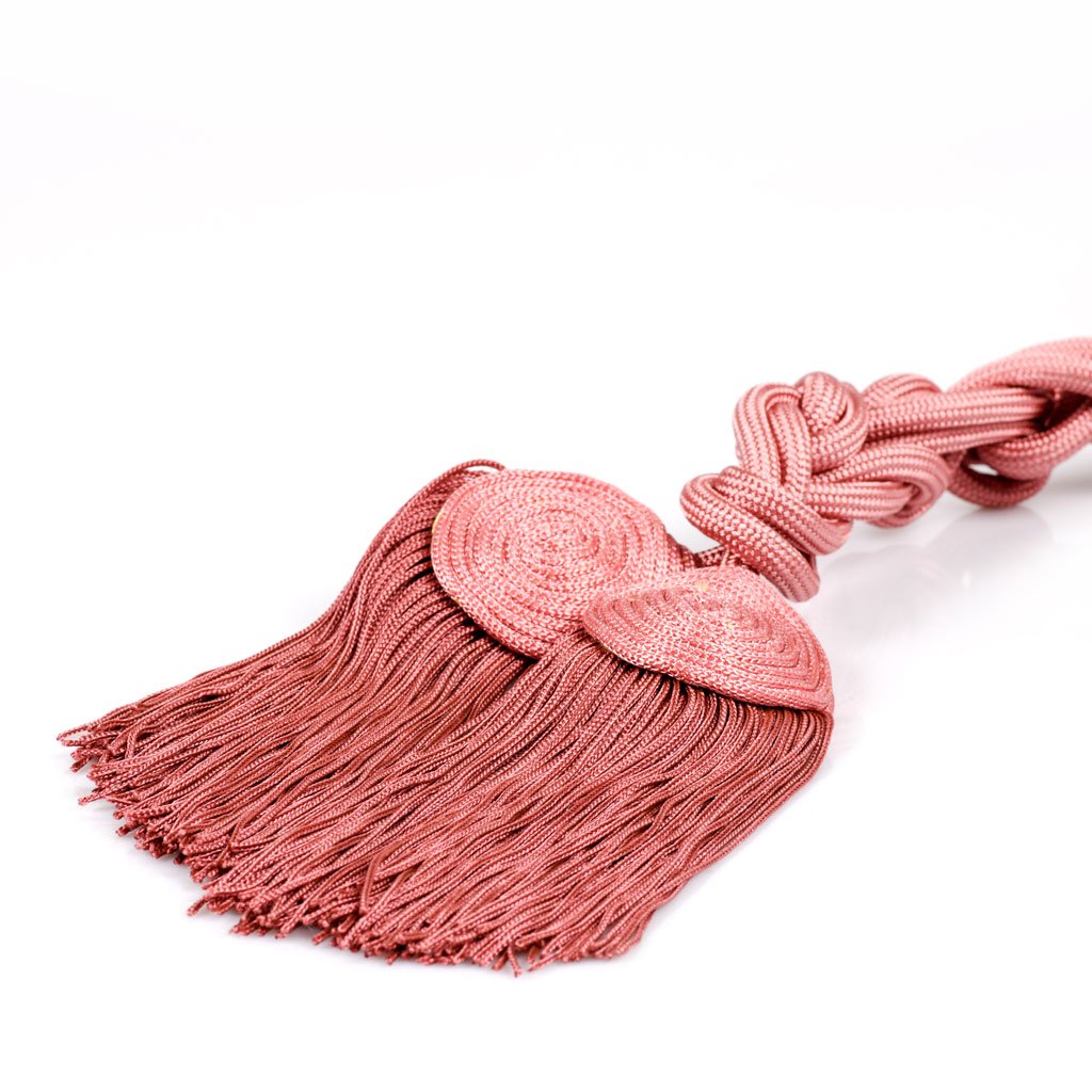 Cingolo Fiocco Piatto: Nappina decorativa rosa con cordoncino intrecciato e due accenti circolari intrecciati, che ricordano un cingolo della sartoria Gammarelli, su sfondo bianco.