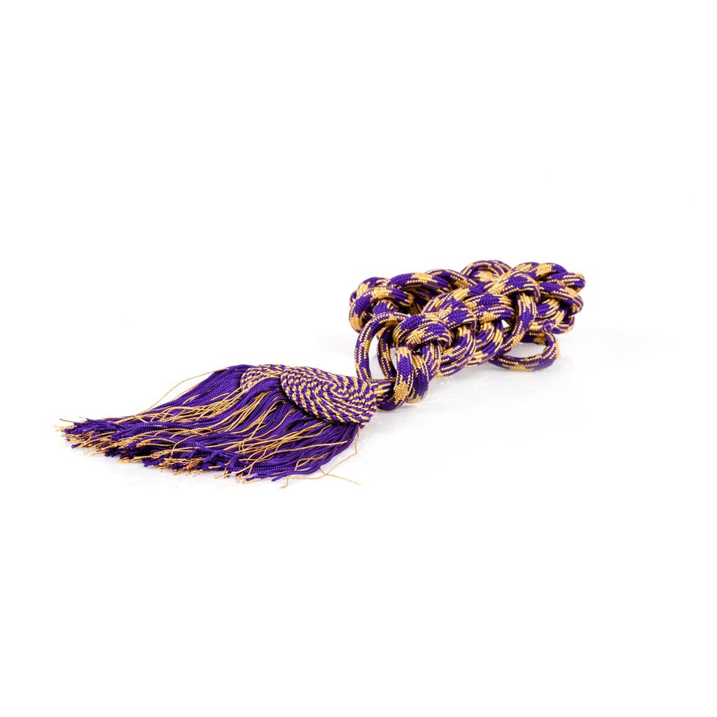 Il Cingolo Piatto Misto Oro o Argento, un cordone decorativo arrotolato di colore viola e oro con estremità a nappina, è raffigurato su uno sfondo bianco.