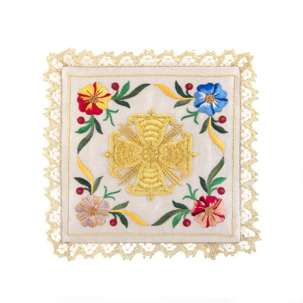 Palla con Croce e Motivi Floreali: telo quadrato ricamato in bianco con una croce dorata, disegni floreali colorati e bordi in pizzo.