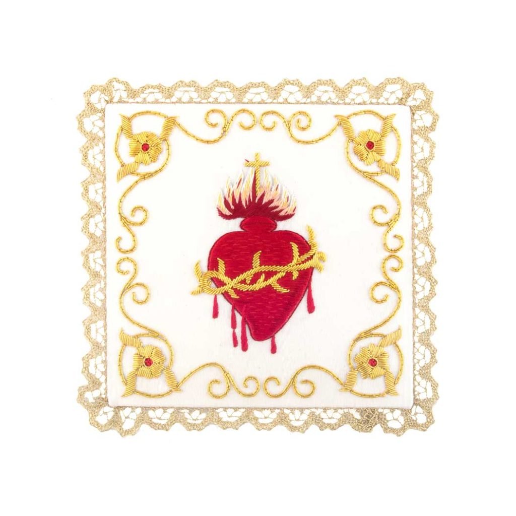 La Palla con Sacro Cuore presenta un cuore rosso ricamato con fiamme e spine dorate, bordato da un ornato pizzo dorato su tessuto bianco.