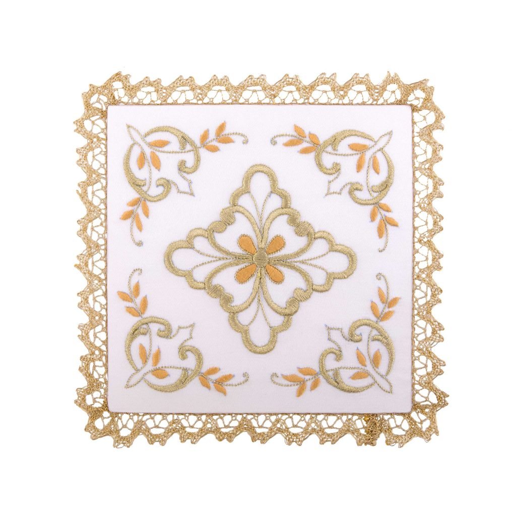 La Palla con Margherita è un centrino quadrato in pizzo bianco con finiture dorate e un motivo floreale ricamato in oro e beige.