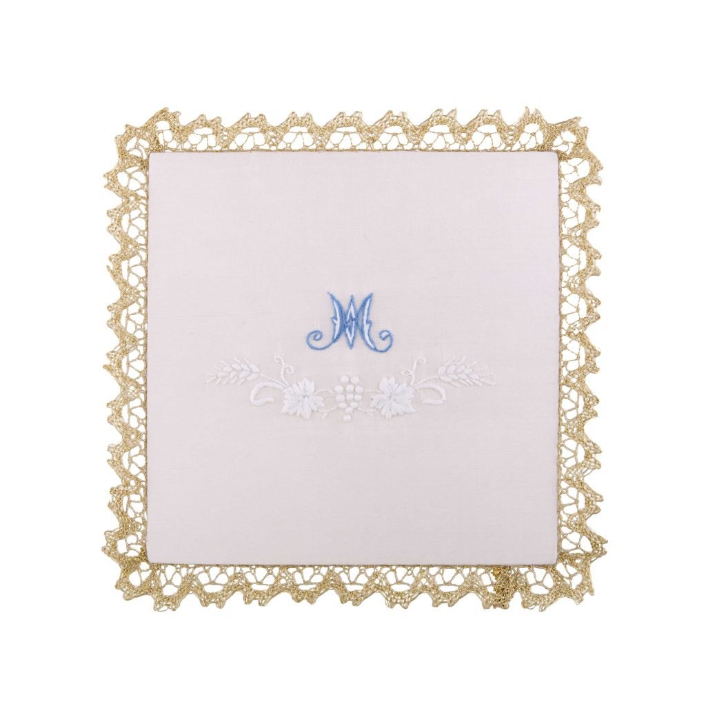 Palla quadrata bianca con Ricamo Mariano Grano e Uva con bordo in pizzo dorato, monogramma M blu e ricamo floreale bianco al centro.