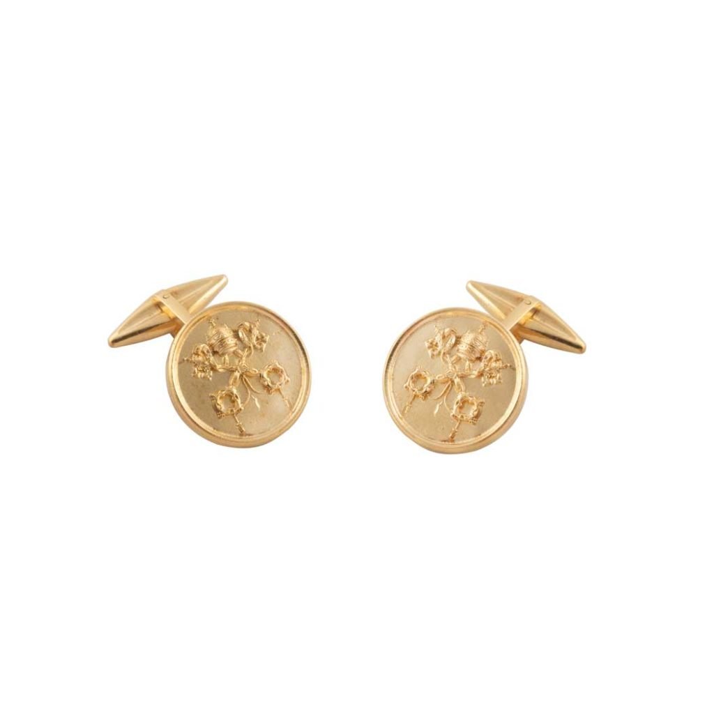 I gemelli tondi in oro Gemelli Chiavi e Tiara sono caratterizzati da un disegno floreale in rilievo, che conferisce eleganza a qualsiasi look ispirato alla tiara. Su sfondo bianco.