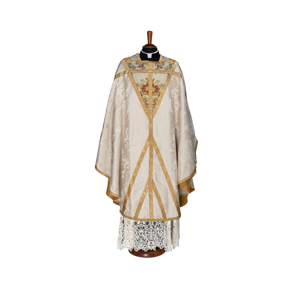 La Casula San Tommaso Becket, in avorio e oro con un disegno floreale ricamato, è esposta su un manichino che indossa un albetto di pizzo.
