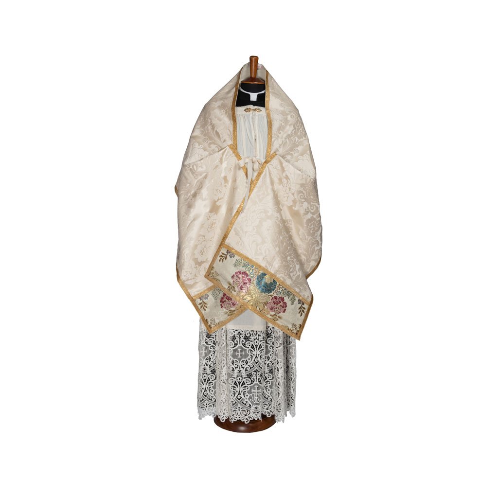 Un manichino vestito con il Velo Omerale Damasco Vaso Romano Inserti Broccato Savoia, uno scialle color crema con ricami floreali e finiture dorate, sopra un abito di pizzo bianco.