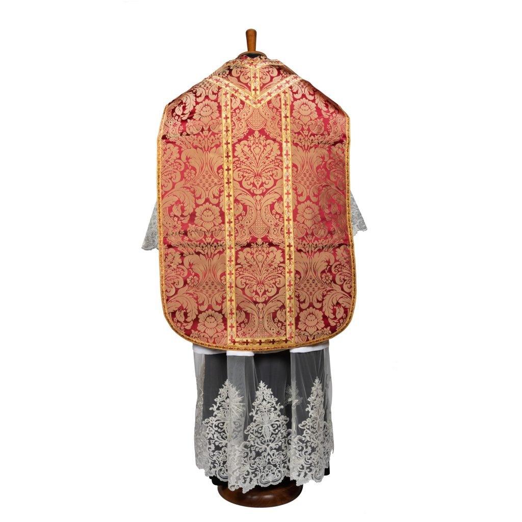 La casula Pianeta Romana Damasco 708, ornata di rosso e oro con pizzo bianco alb di Gammarelli Sartoria, è esposta su un manichino e vista dal retro.