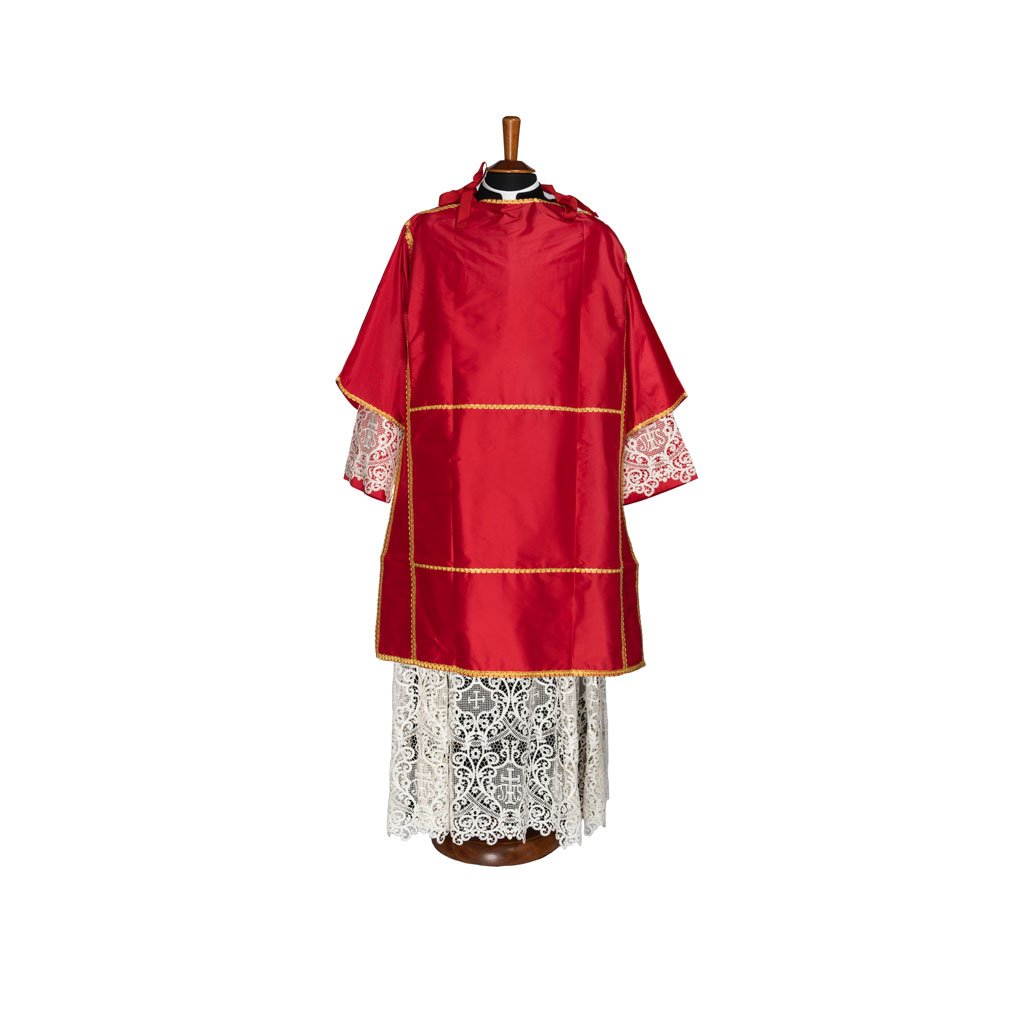 Dalmatica Pontificale in Seta Cremisi con finiture dorate, indossata su una veste di pizzo bianco ed esposta su un manichino su sfondo bianco.