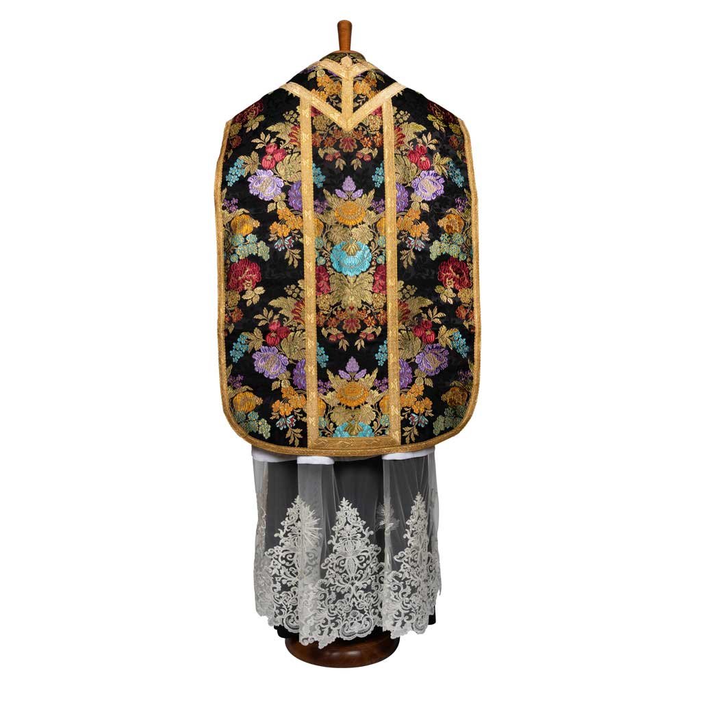 Un paramento Pianeta Romana Broccato Savoia in nero e oro con ricami floreali colorati, esposto su un manichino.