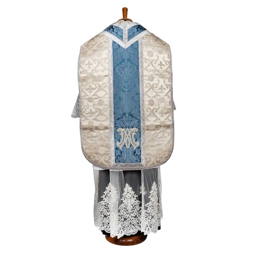 La Pianeta Romana Damasco San Luigi con Inserti di Gammarelli Sartoria è caratterizzata da un broccato bianco e blu con motivi intricati, esposto su un supporto ed elegantemente rifinito con un pizzo sul fondo.