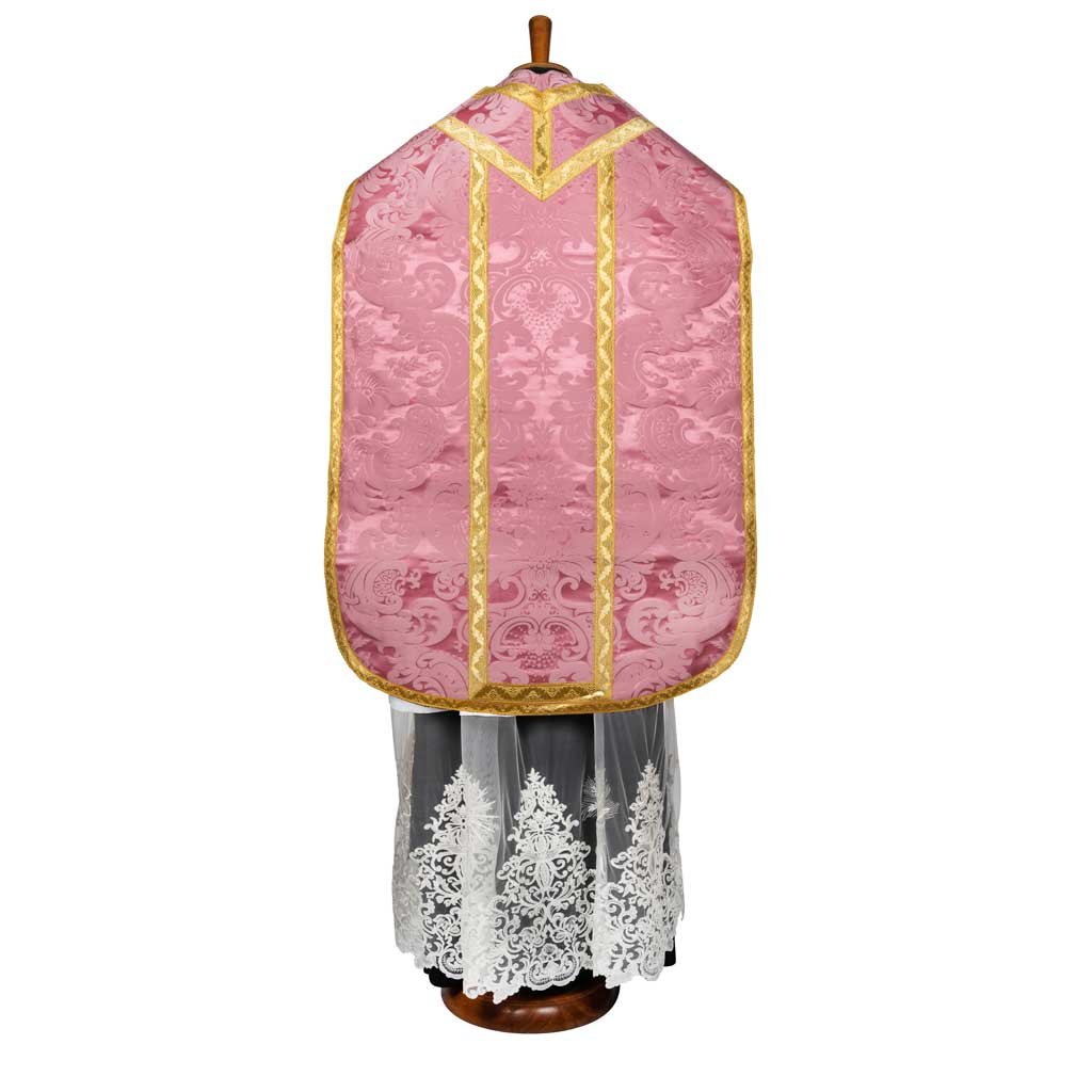 La Pianeta Romana Damasco Nocca di Gammarelli Sartoria, in rosa e oro, è esposta su un cavalletto, drappeggiata su un capo di pizzo bianco e mostrata dal retro.