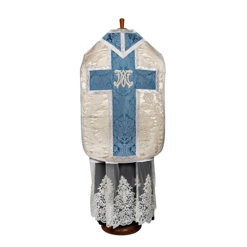Il Pianeta Romana Damasco Vaso Romano con Inserti, un paramento ornato di blu e bianco con un disegno a croce, è esposto su un manichino.
