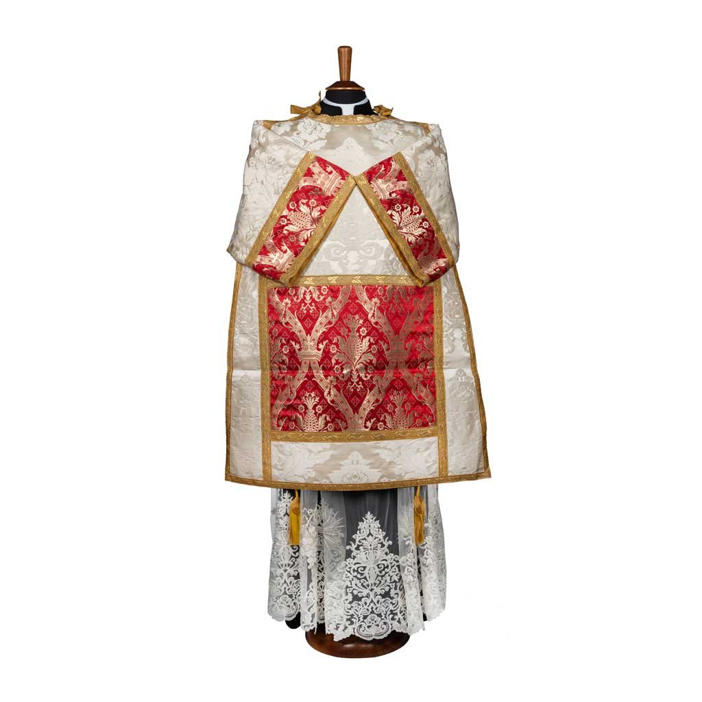 La Tonacella Stile Romano Damasco Vaso Romano, un paramento cattolico tradizionale in bianco e rosso con dettagli in pizzo, è esposta su uno stand.