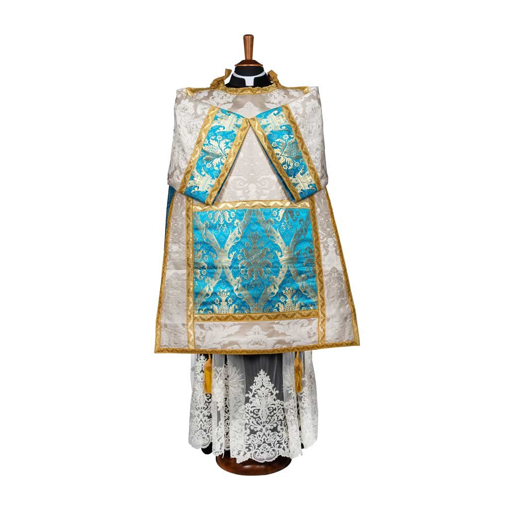 La Tonacella Stile Romano Damasco Vaso Romano è un paramento bianco e oro con accenti blu e motivi intricati, esposto su un manichino.