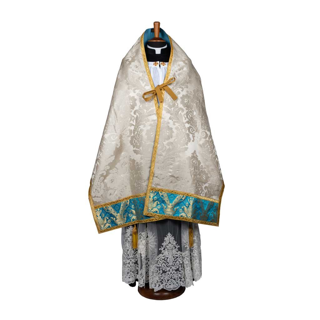 Il Velo Omerale, un tradizionale mantello di broccato bianco e oro con finiture blu, è esposto su una forma di abito.