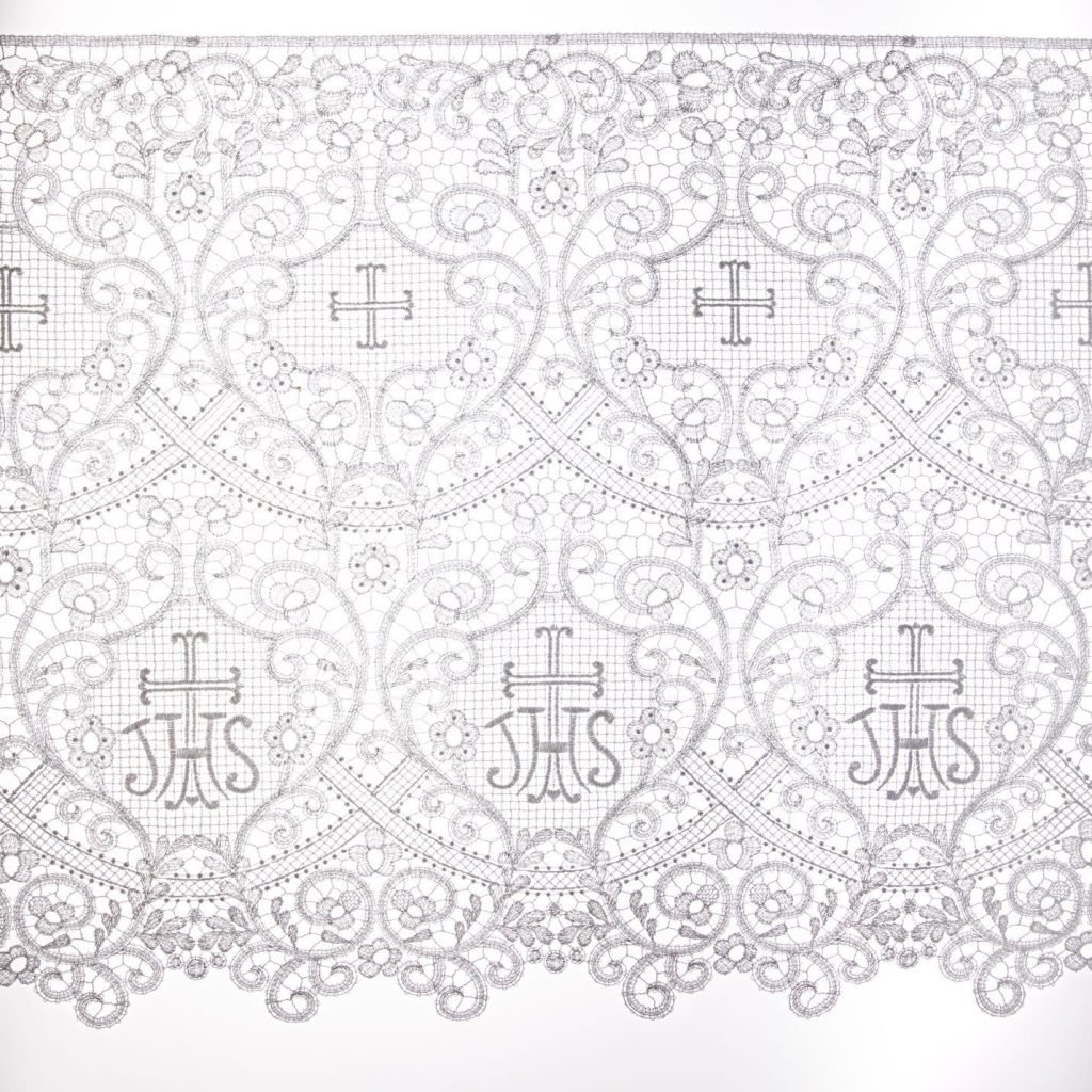 Il Merletto Macramè con IHS è caratterizzato da un intricato pizzo bianco con motivi floreali, croci e monogrammi religiosi "IHS".
