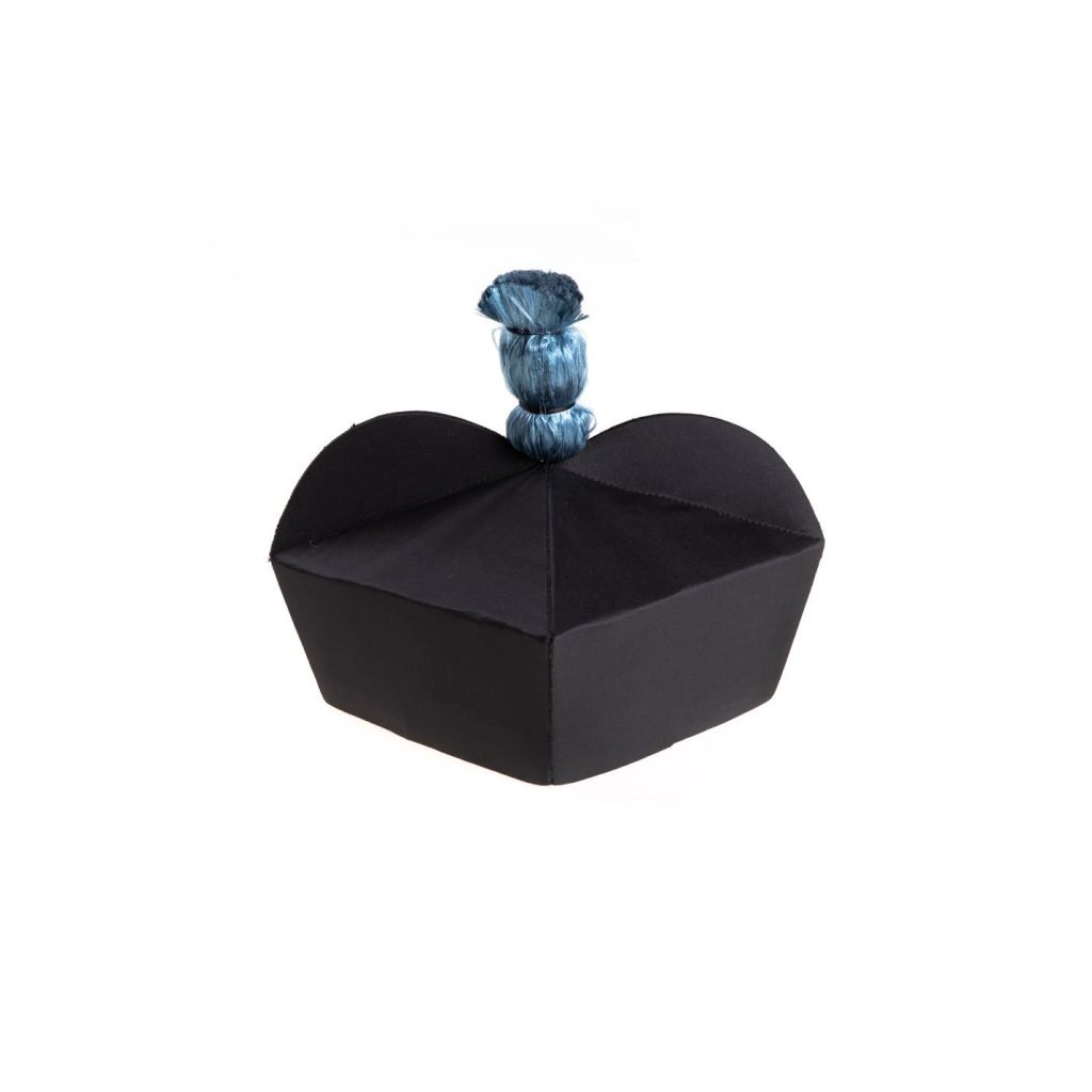 Berretta in Seta con Fodera e Fiocco Blu del Re: un cappello geometrico di seta nera con un nodo decorativo blu sulla sommità, su sfondo bianco.