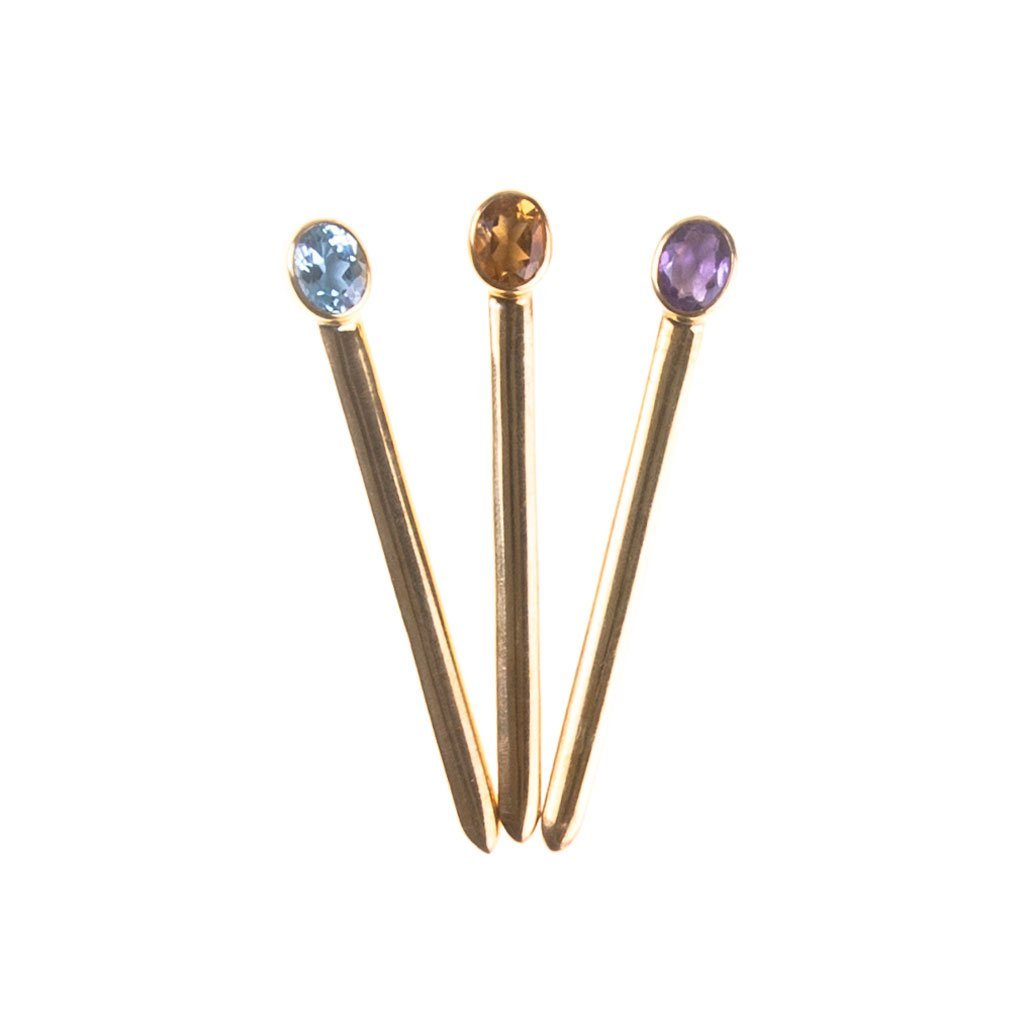 Tre spille Acicule Classiche in oro, ciascuna sormontata da una gemma blu, arancione o viola, sono disposte a ventaglio su sfondo bianco.