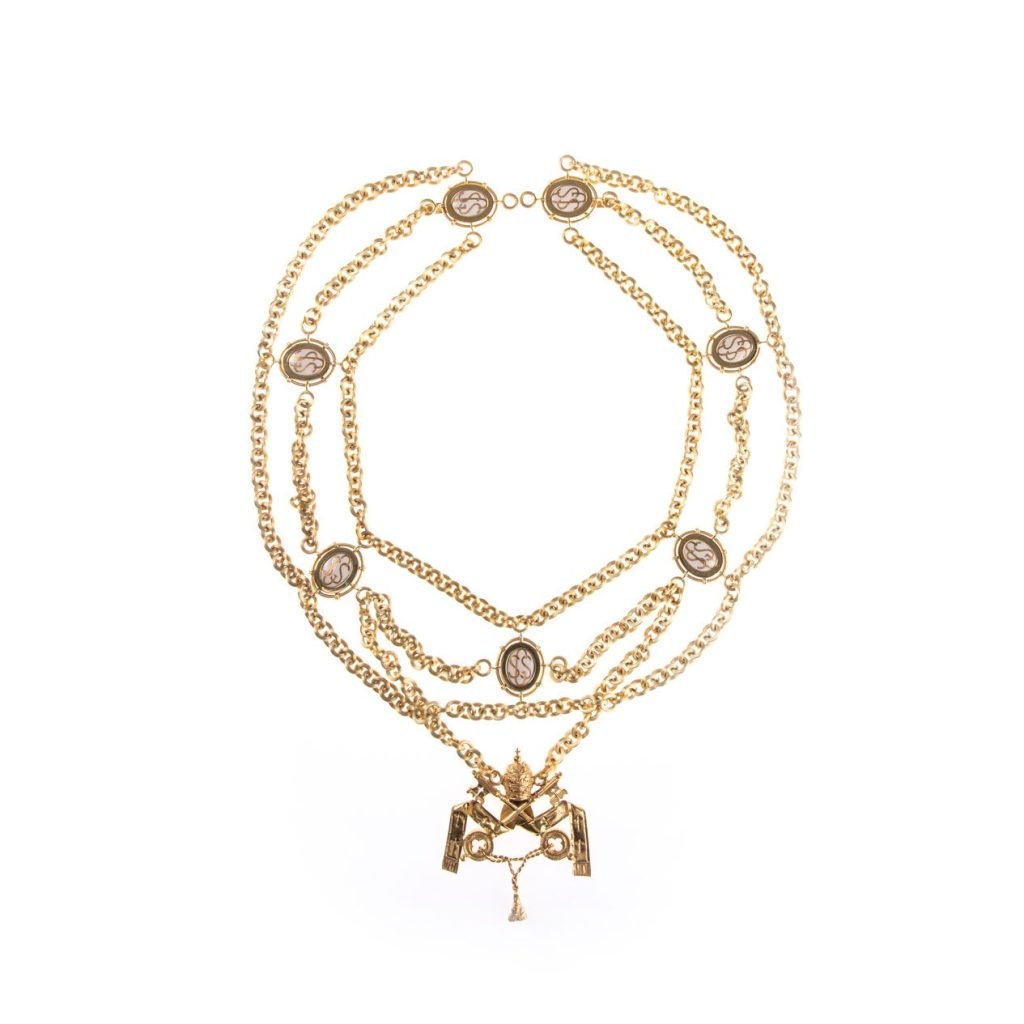 La Collana per Gentiluomo di Sua Santità è una collana d'oro a più catene con ciondoli a cammeo e un pendente centrale ornato, su sfondo bianco.