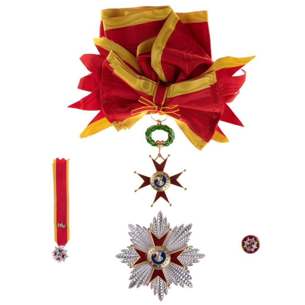 Nastro da cerimonia rosso e oro con medaglie e insegne a forma di stella, con emblemi centrali blu, che rappresenta la Decorazione per Cavaliere Gran Croce Ordine San Gregorio Magno.